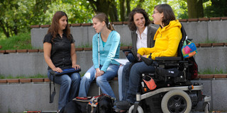 Studierende mit Behinderung Vier Studierende, darunter Studierende mit Behinderung, sitzen gemeinsam auf dem Campus.